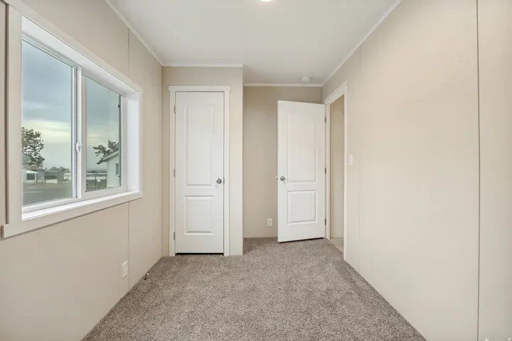 Interior space featuring neutral tone wall panels, light brown carpeting, a sliding window with white trim, and two paneled interior doors