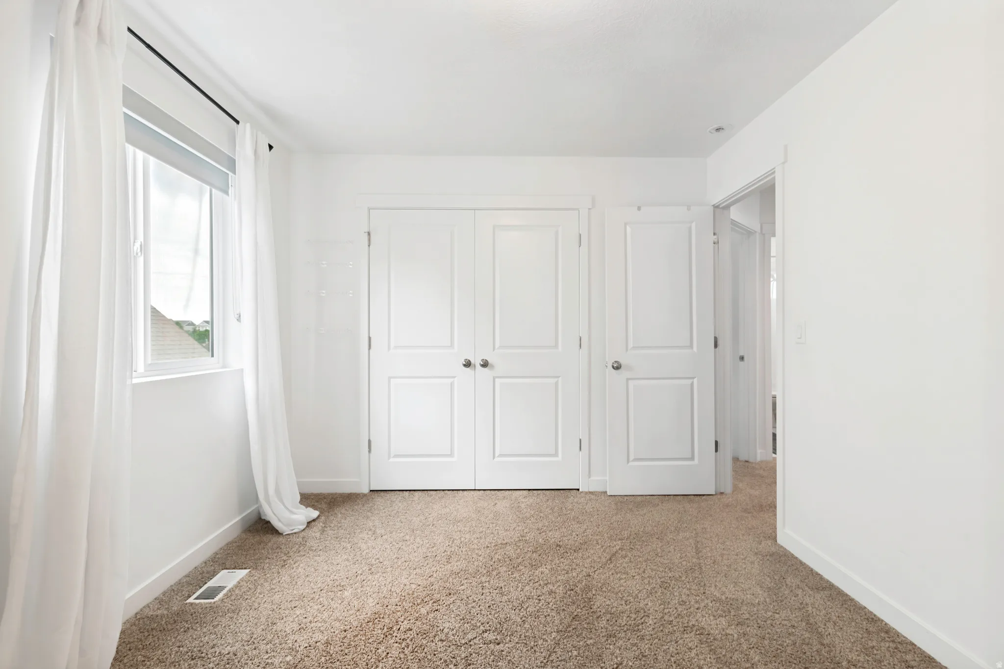 Carpeted room featuring a white-framed window, bright white walls, and a pair of white bi-fold doors