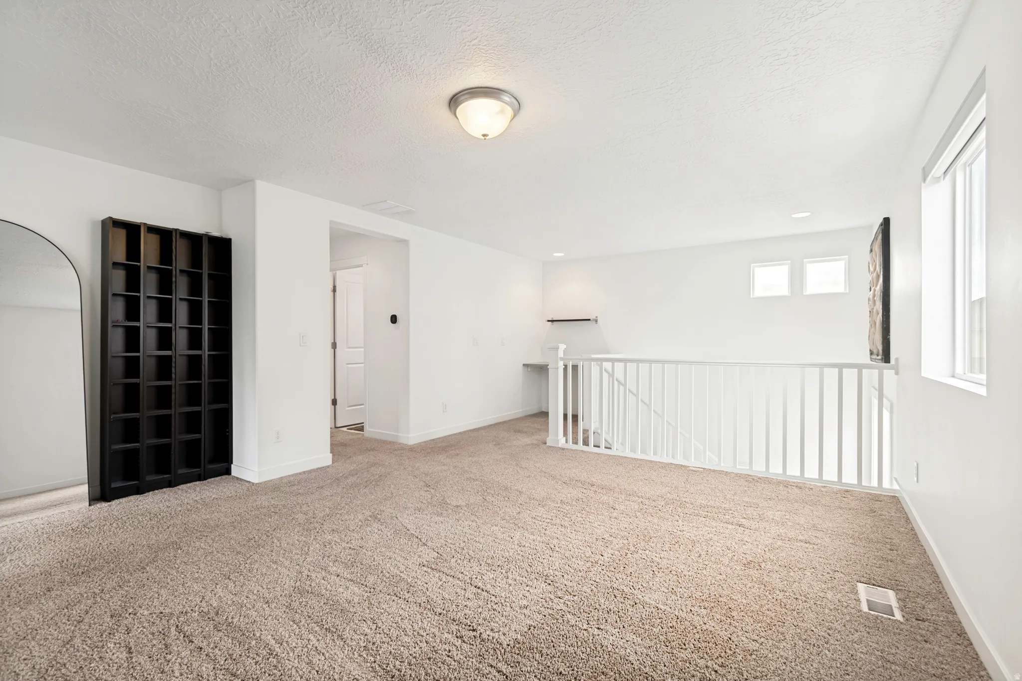 Spacious upper-level landing featuring neutral carpet, white walls, and a built-in shelving unit