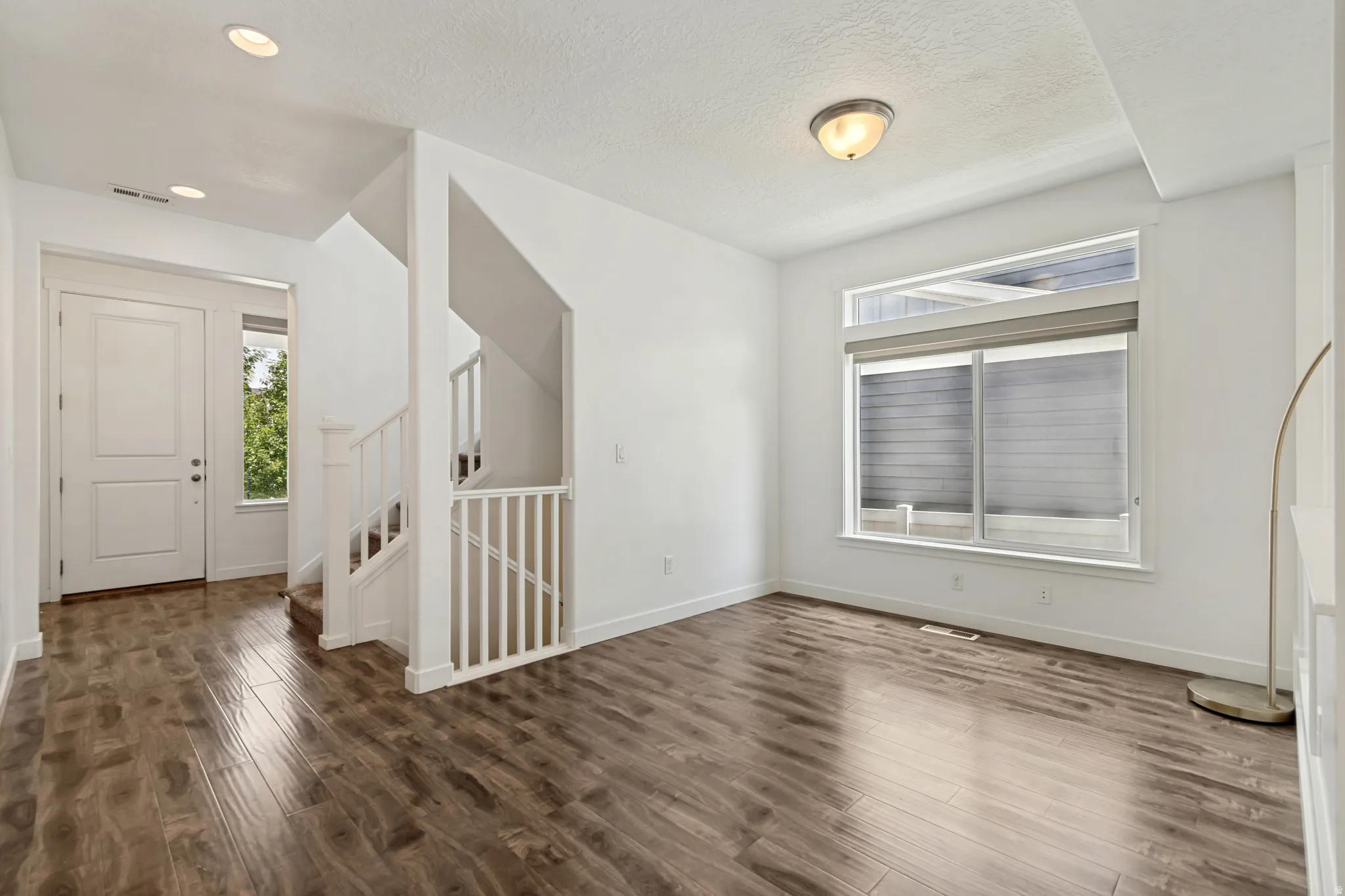 Bright entry area featuring wood-finish flooring, white paneled door, large windows with upper transom, and a staircase with white balusters