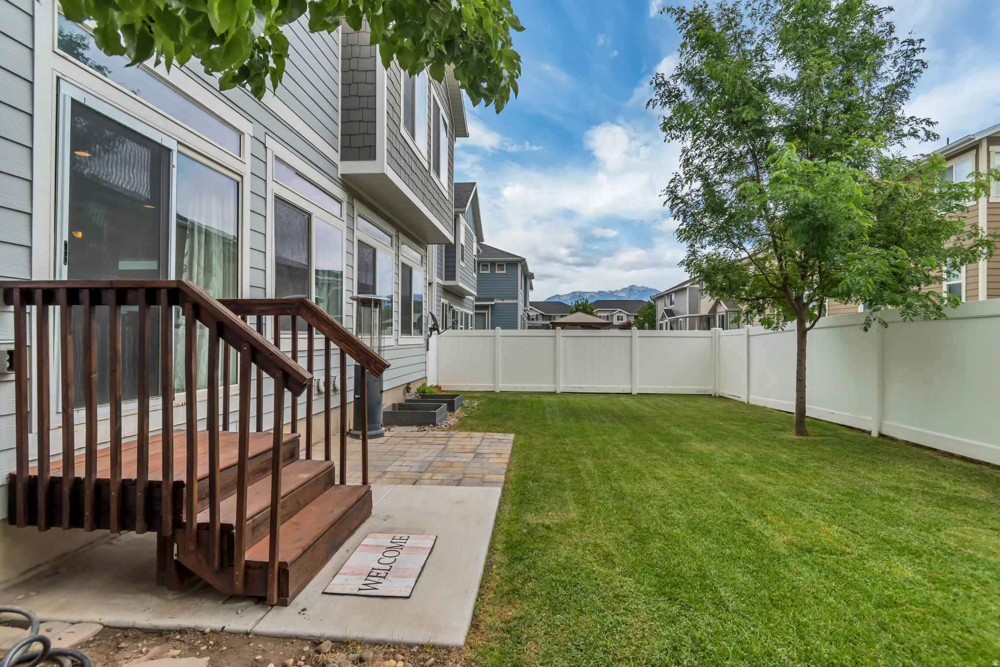 Expansive backyard featuring a manicured lawn, a mature tree, and a white privacy fence