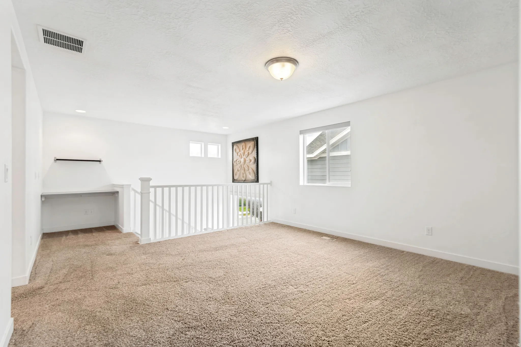 Carpeted loft area featuring a built-in desk with shelving, a white railing, and multiple windows providing natural illumination