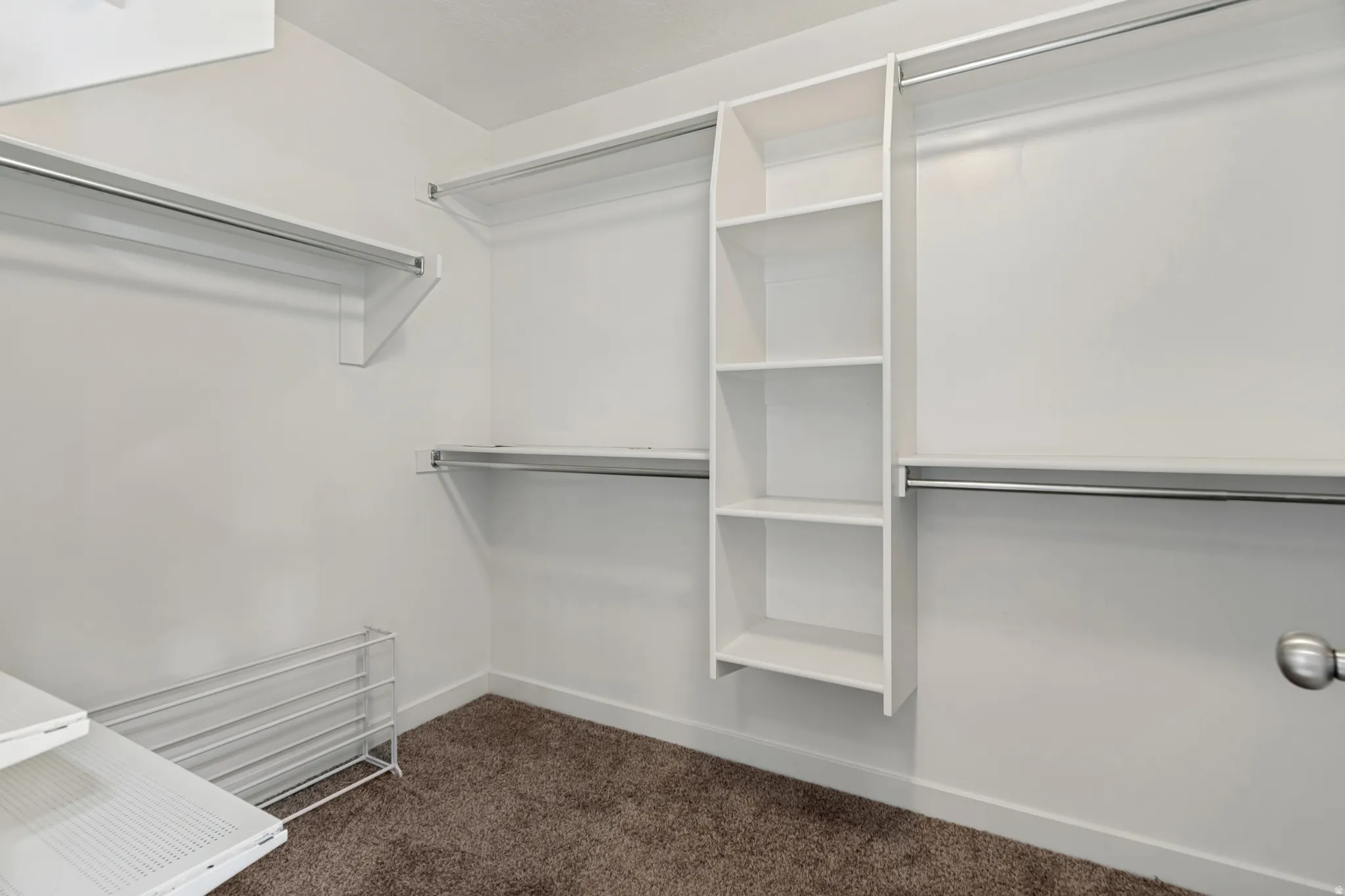 Walk-in closet featuring built-in shelving, multiple hanging rods, and dark brown carpeting