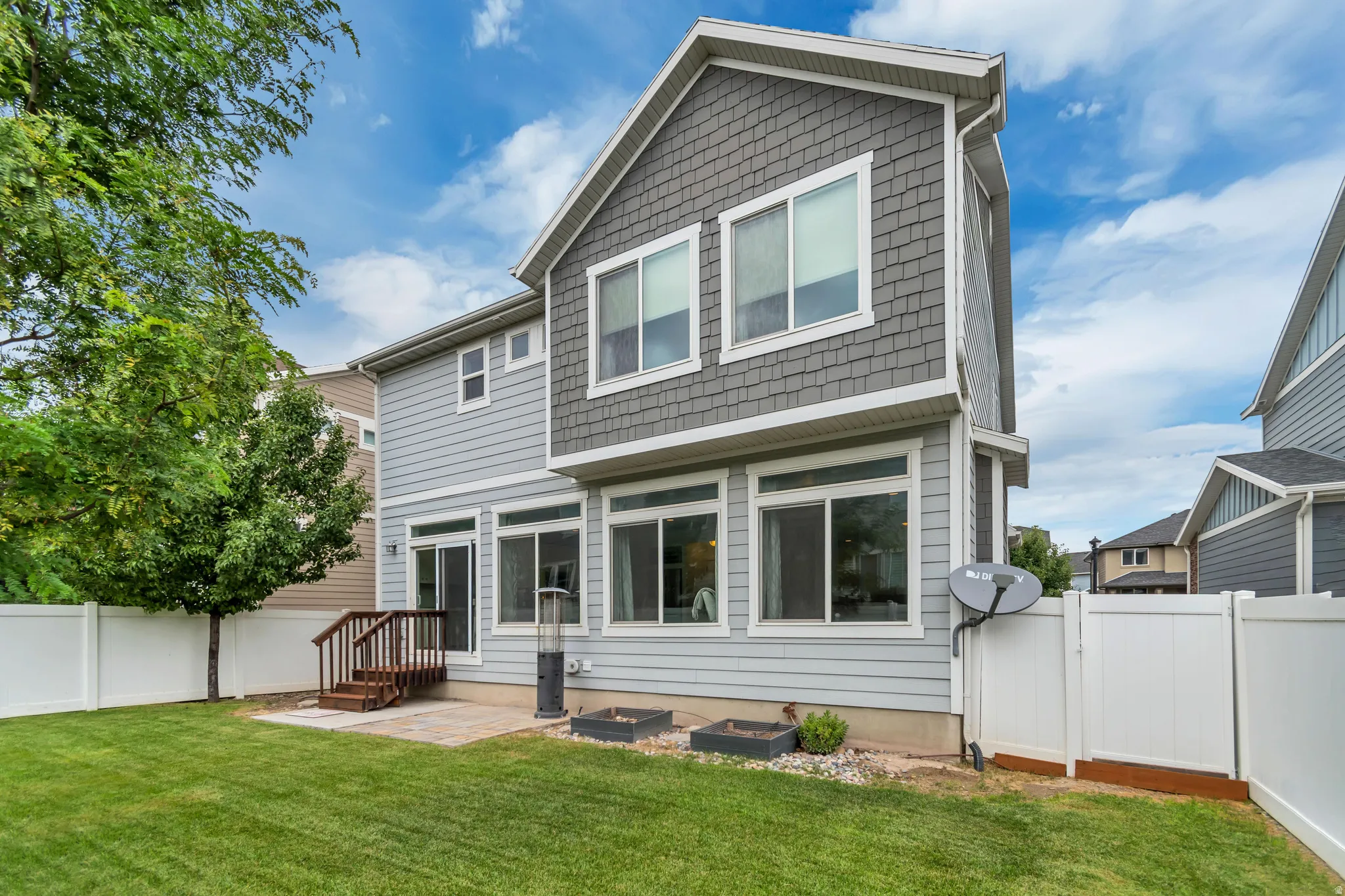 Fenced backyard featuring a paver patio with wood steps, extensive green lawn, and mature trees