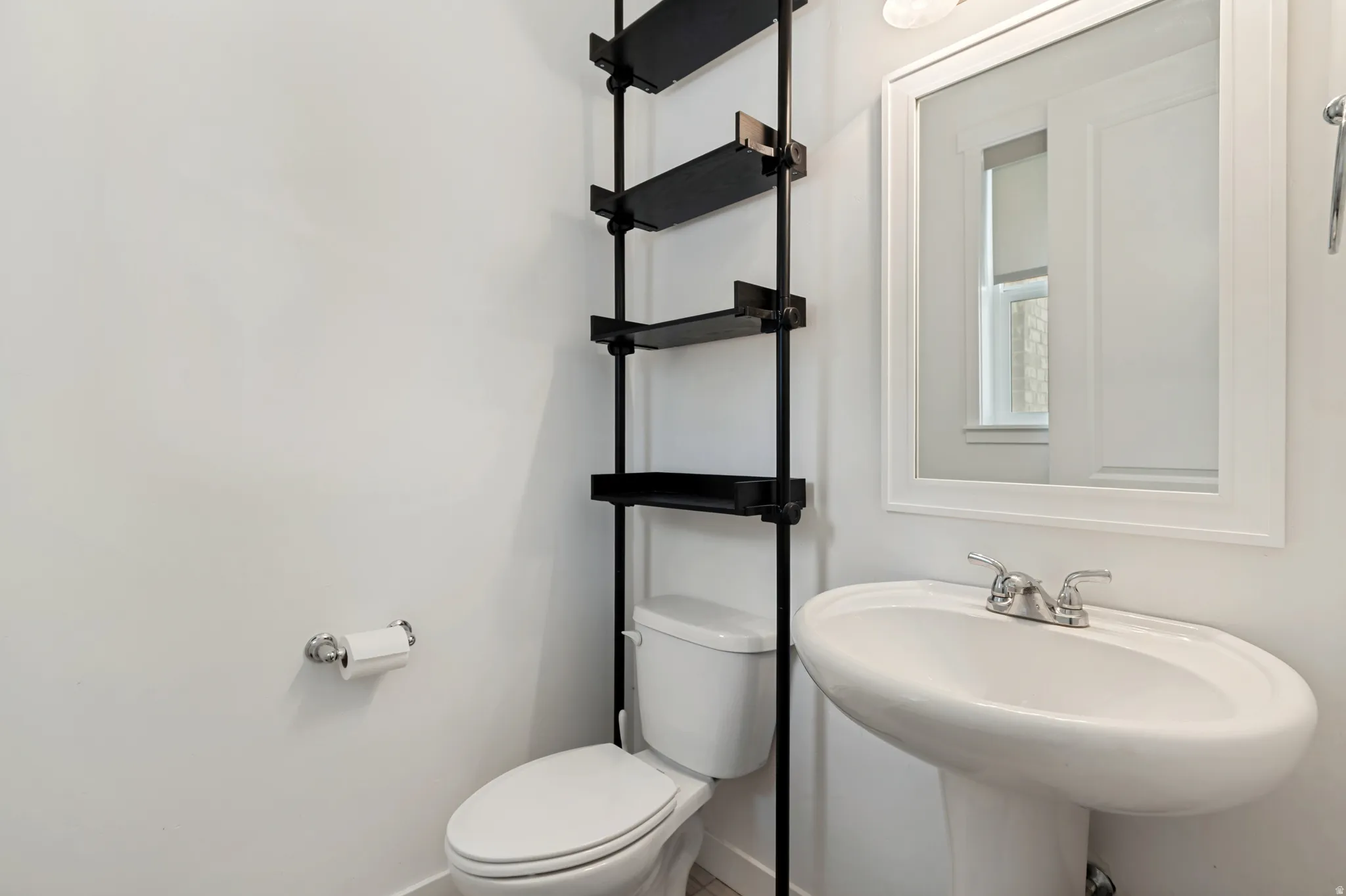 Pedestal sink with chrome faucet, framed mirror, and built-in shelving