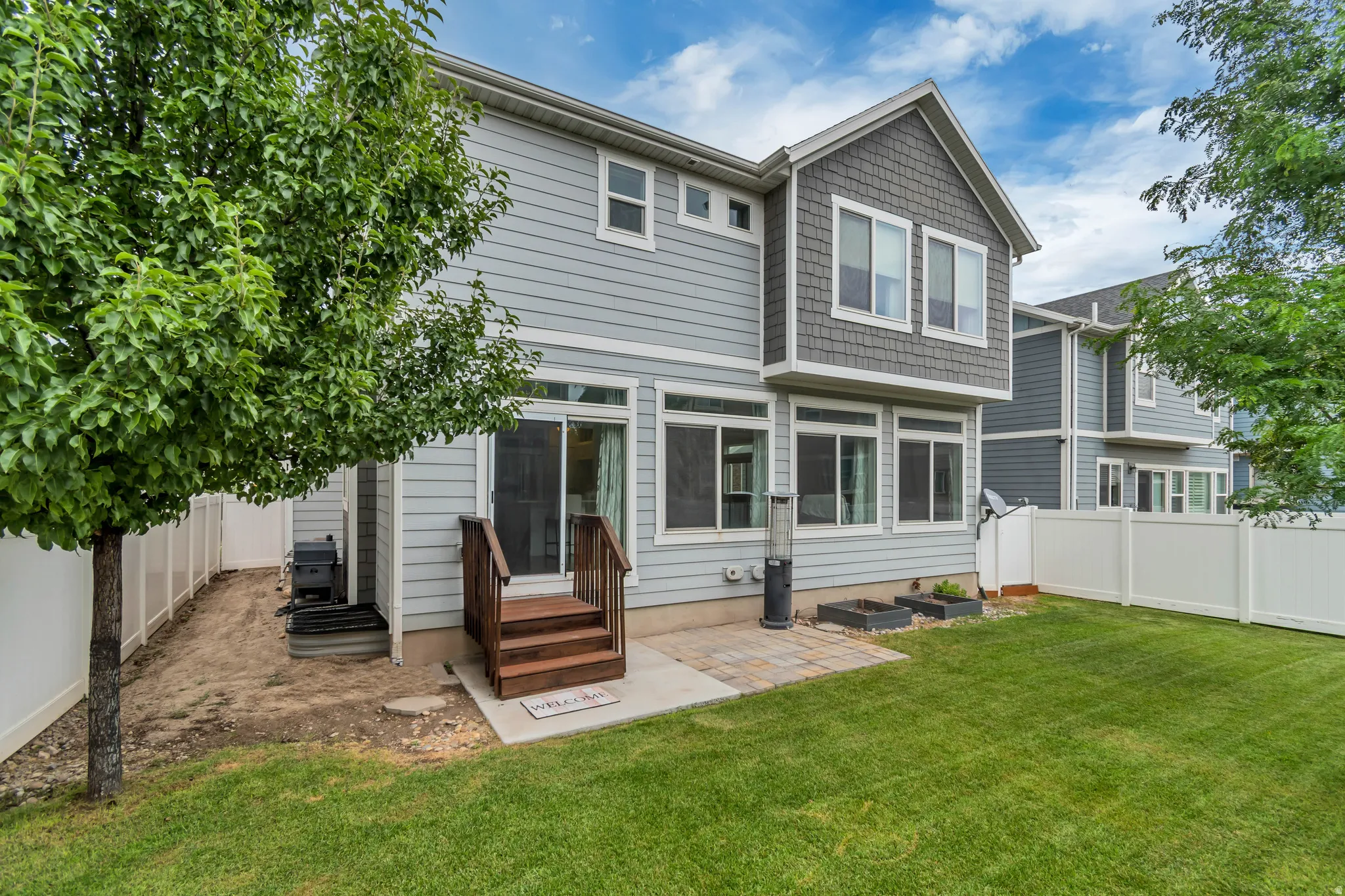 Rear exterior featuring light blue siding with gray shingle accents, a white vinyl fence, and a green lawn