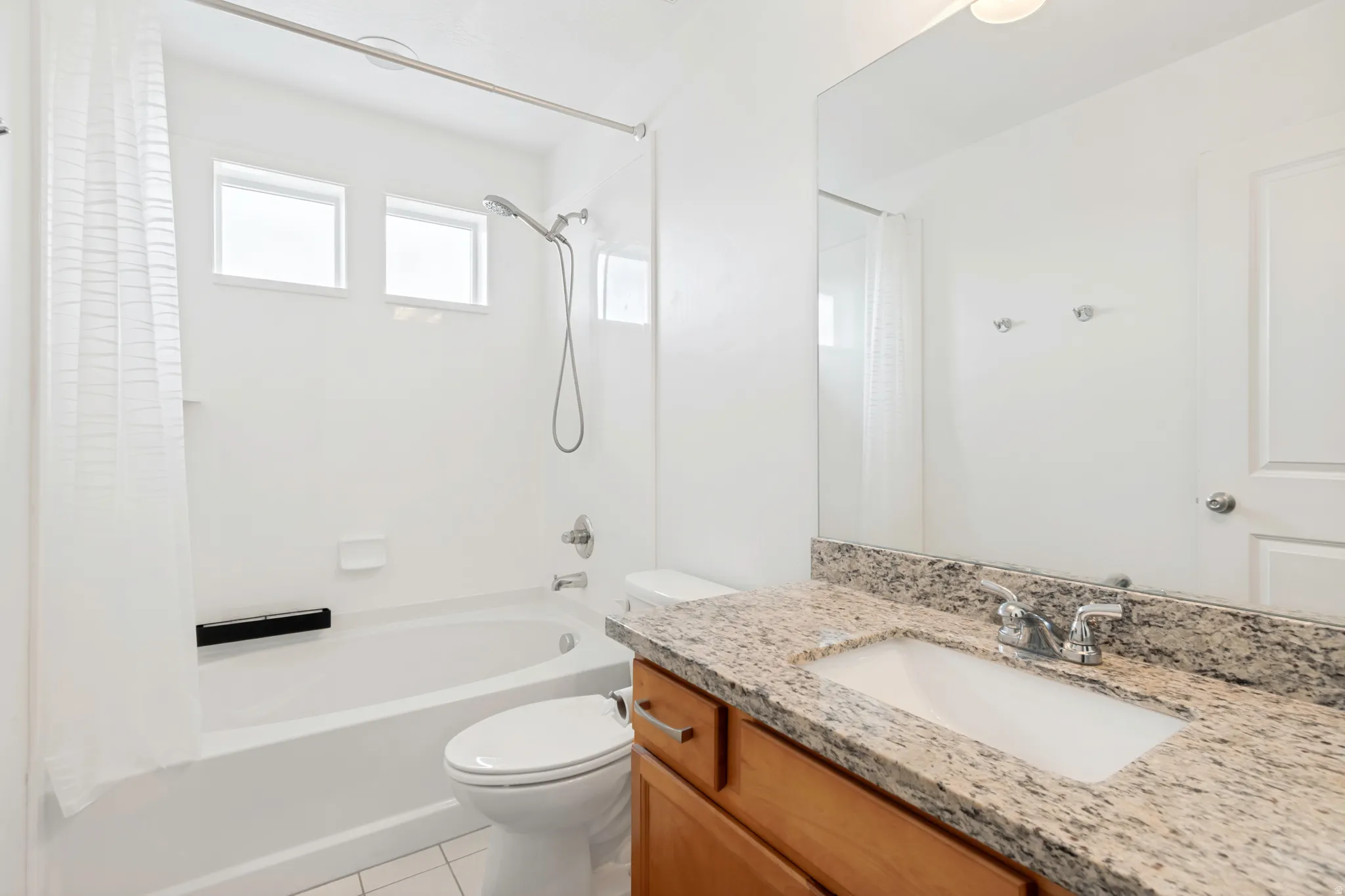 Bathroom featuring a bathtub with shower fixture, dual transom windows, a toilet, and a vanity with an integrated sink and stone-finish countertop