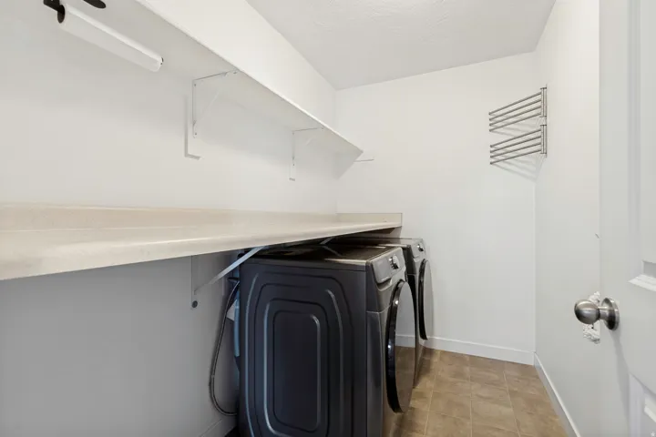 Laundry area featuring a built-in countertop, two white storage shelves, and a wall-mounted drying rack