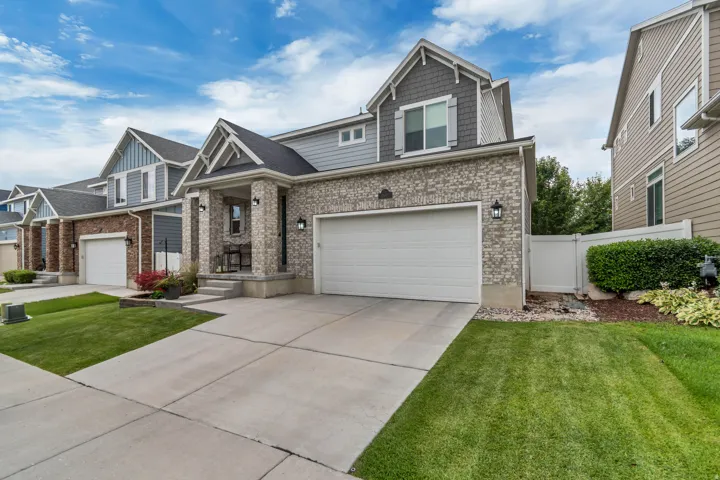 Contemporary two-story residence featuring a brick and siding exterior, an attached garage, a covered front porch, a well-maintained lawn, and a paved driveway