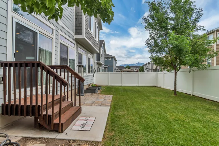 Expansive backyard featuring a manicured lawn, a mature tree, and a white privacy fence