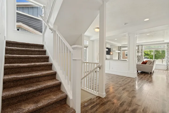 Carpeted staircase with white balusters and handrails, complemented by wood-finish flooring in the adjacent living area