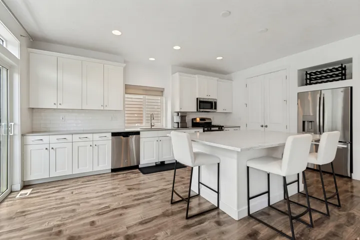Open-concept kitchen featuring an oversized island with seating, white shaker cabinetry, stainless steel appliances, and wood-finish flooring