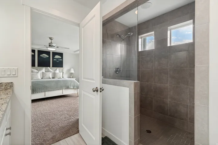 Walk-in shower featuring gray tile surround, glass enclosure, and two high-set windows