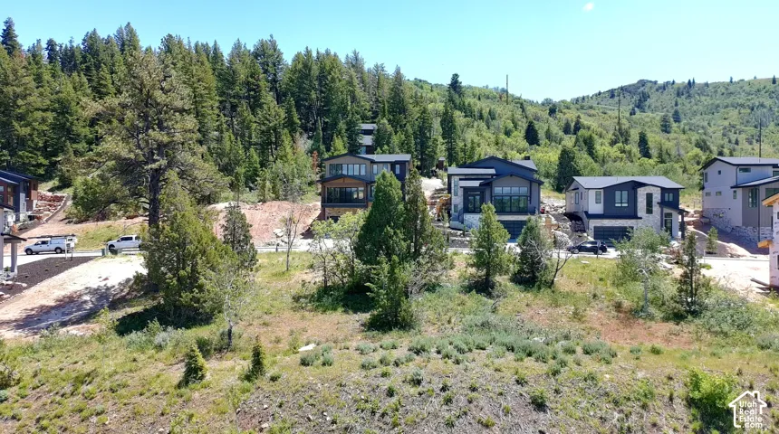 Modern mountain-side residences featuring multi-level designs, expansive window placements, and integrated garages, surrounded by mature trees and natural landscaping