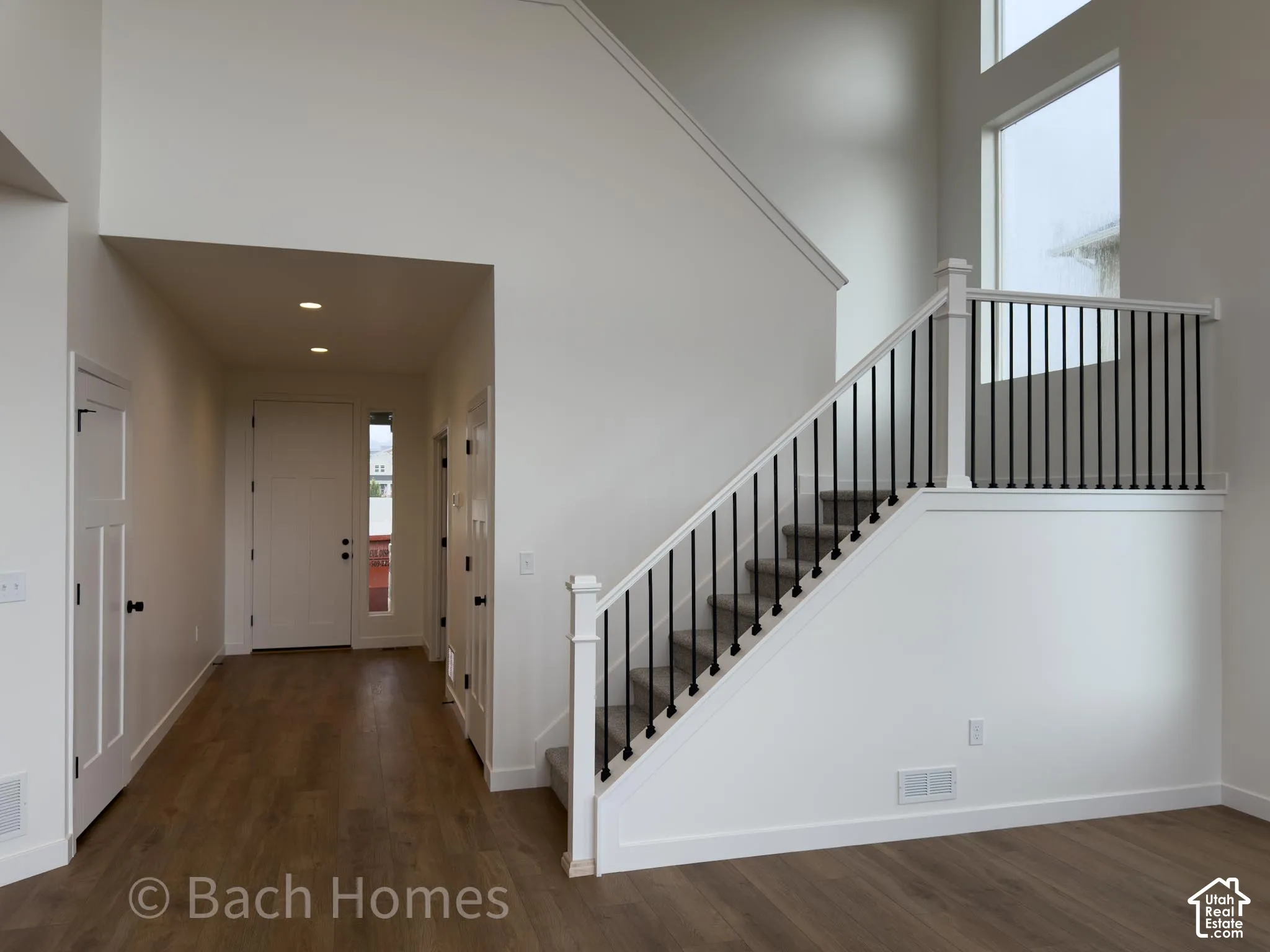 Vaulted ceilings, wood-finish flooring, staircase with black metal balusters, tall windows, and recessed lighting
