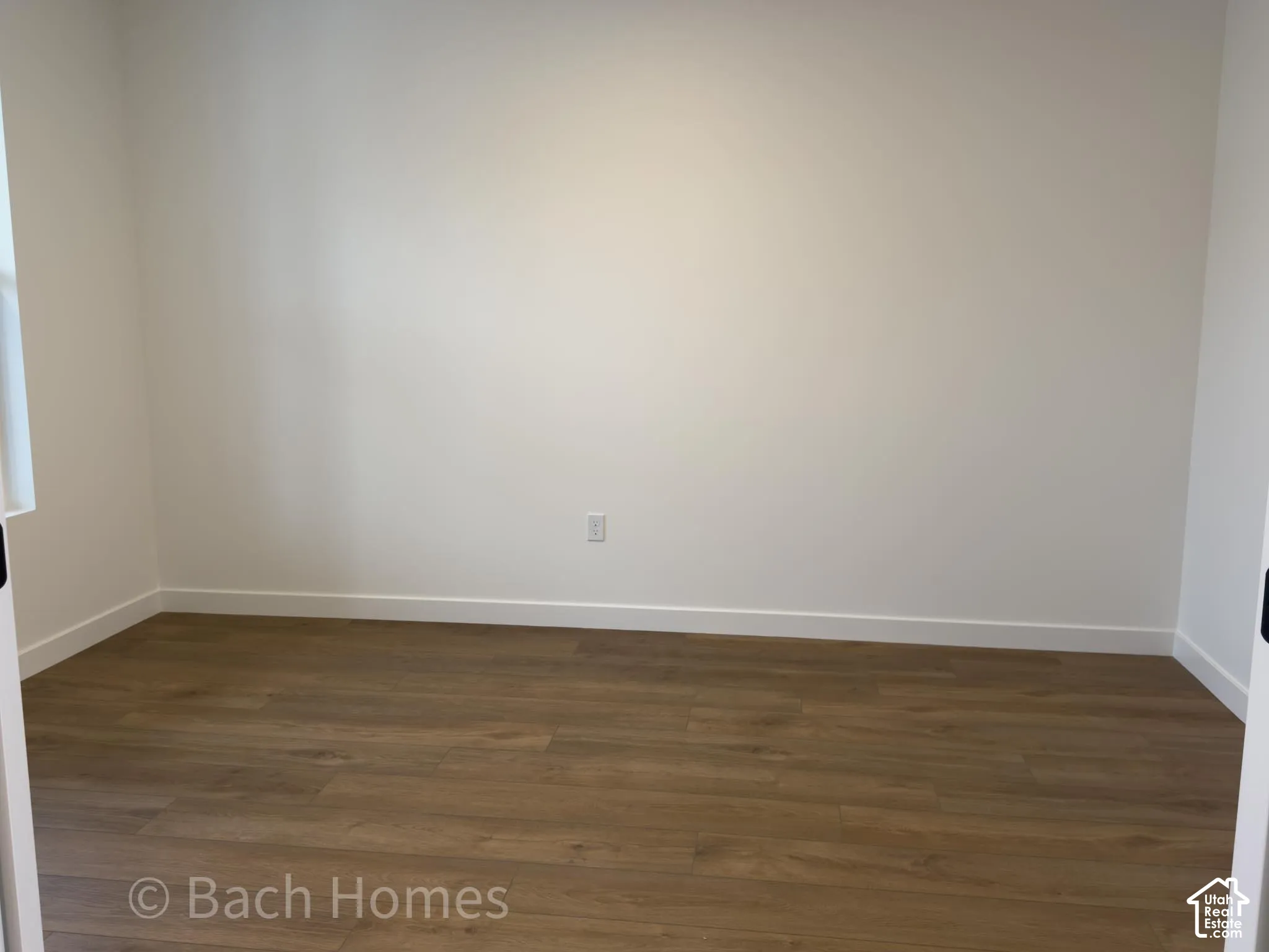 Neutral interior room featuring wood-finish flooring and solid wall surfaces