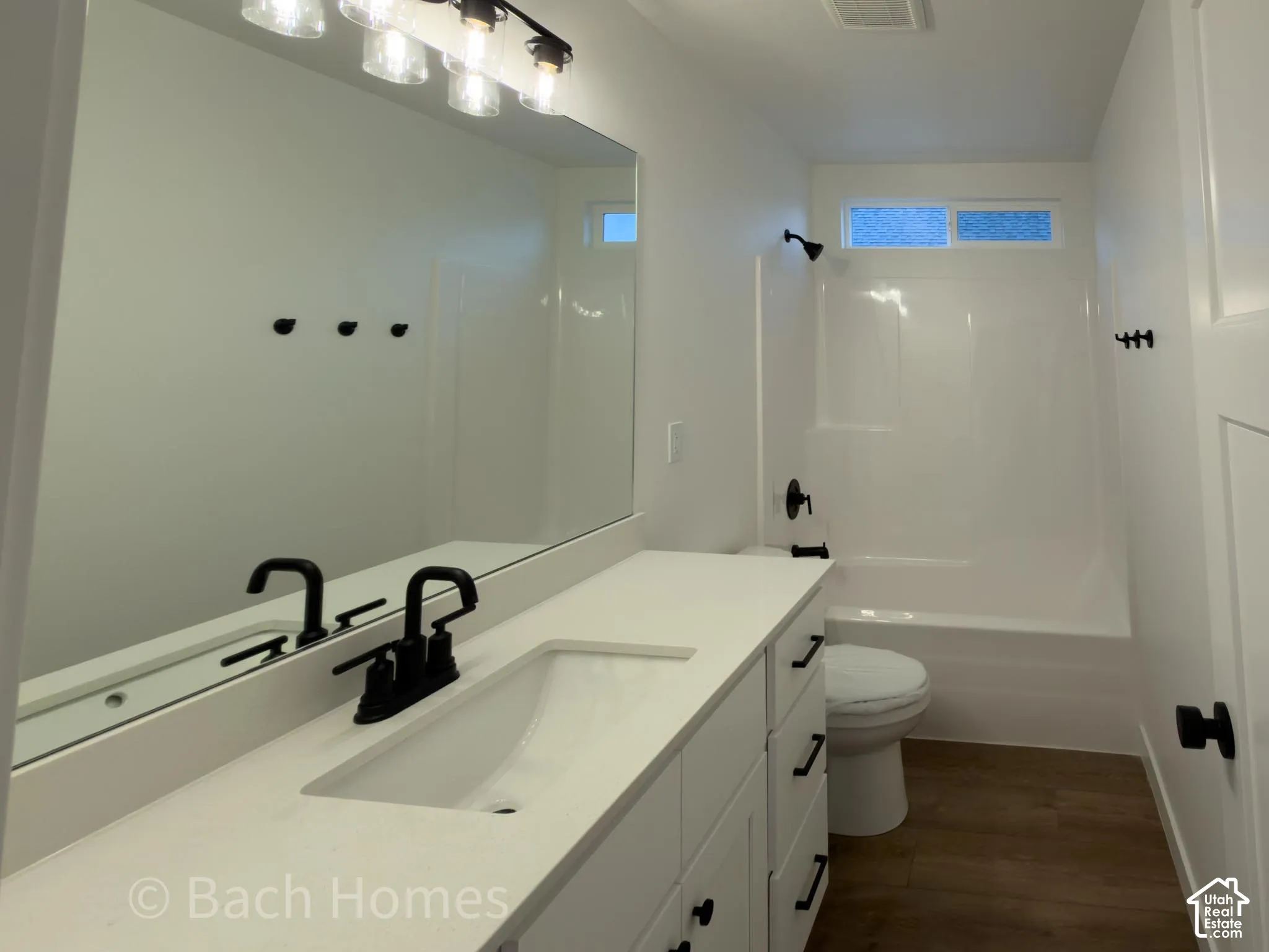 Bathroom featuring a white vanity with a composite countertop, matte black fixtures, full-width mirror, and wood-finish flooring