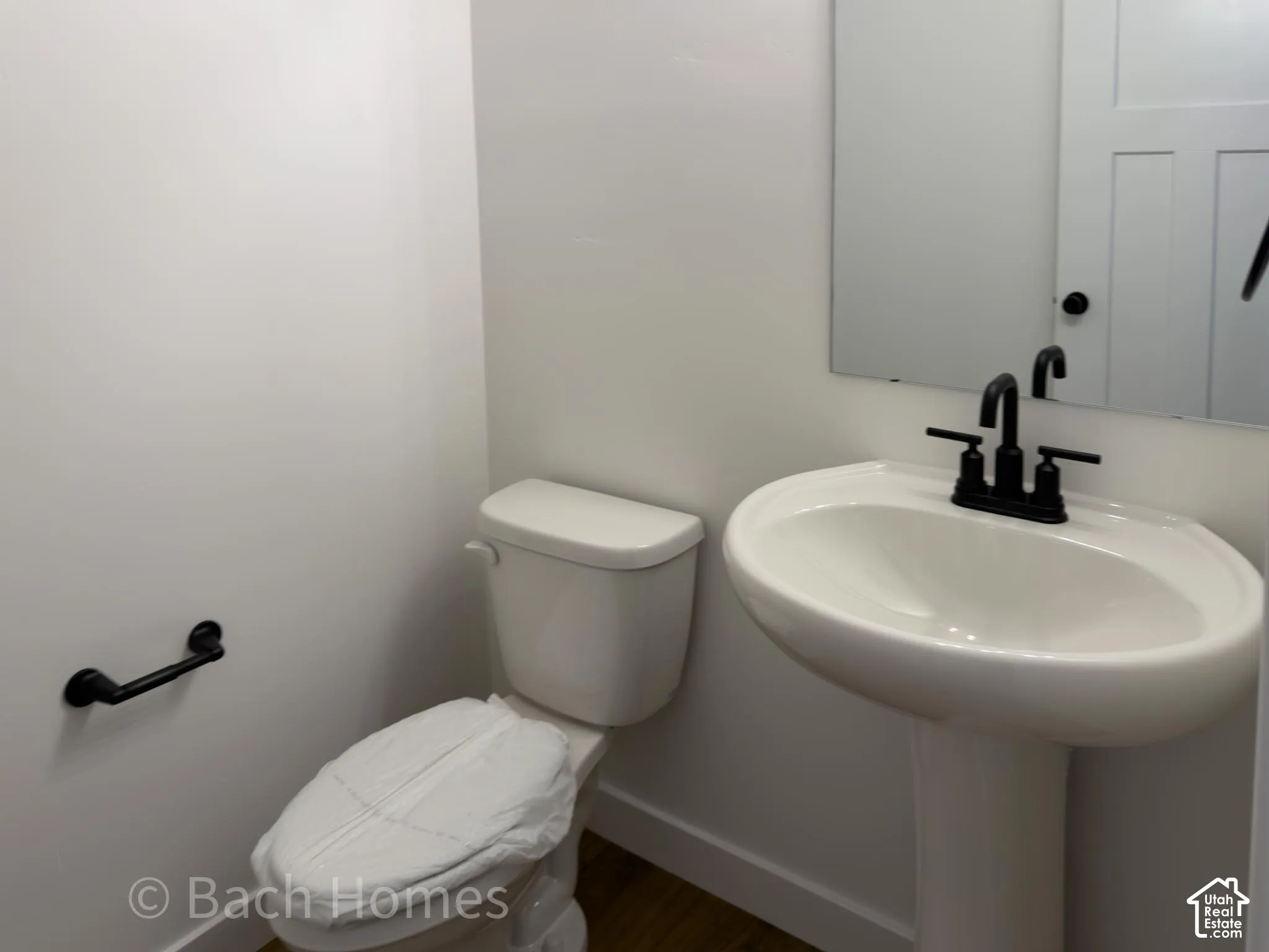 Pedestal sink with matte black widespread faucet, rectangular wall-mounted mirror, and matte black hardware