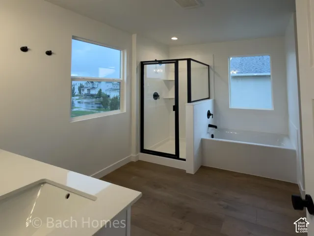Bathroom featuring wood-finish flooring, quartz-surfaced countertop, glass-enclosed shower with matte black hardware, and deep soaking tub