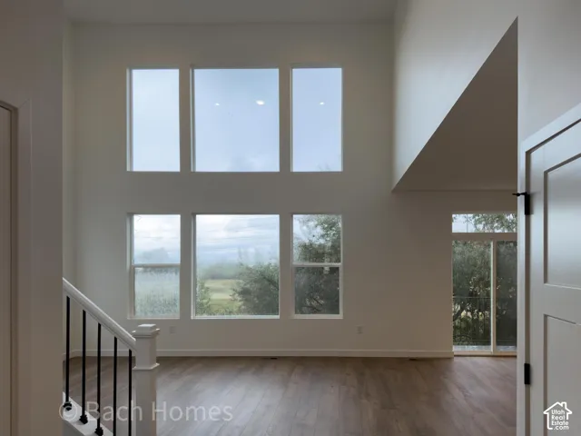 Double-height ceiling featuring a stacked window configuration, wood-finish flooring, and a staircase with a white balustrade and black metal spindles