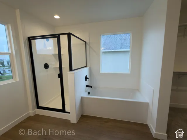 Walk-in shower with matte black framing and fixtures, deep soaking tub, and wood-finish flooring