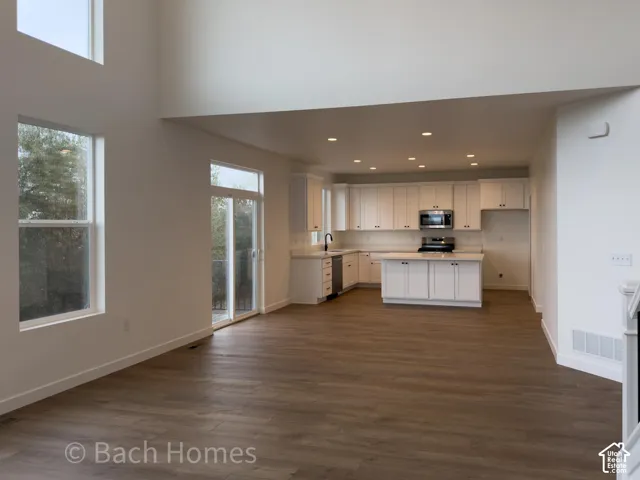 Open-concept space featuring vaulted ceilings, wood-finish flooring, white shaker-style cabinetry, central kitchen island, and recessed lighting