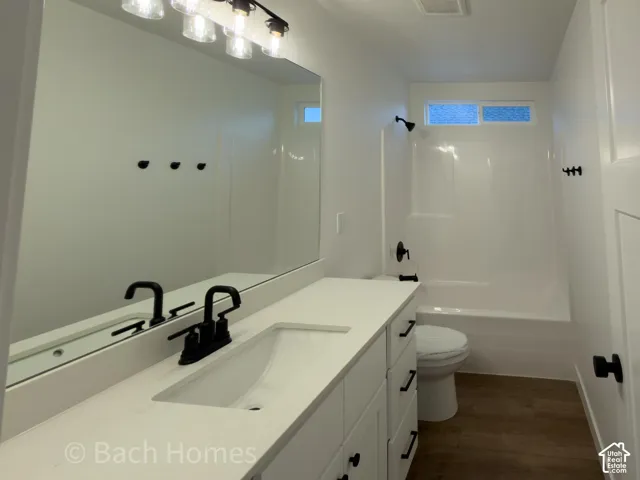 Bathroom featuring a white vanity with a composite countertop, matte black fixtures, full-width mirror, and wood-finish flooring