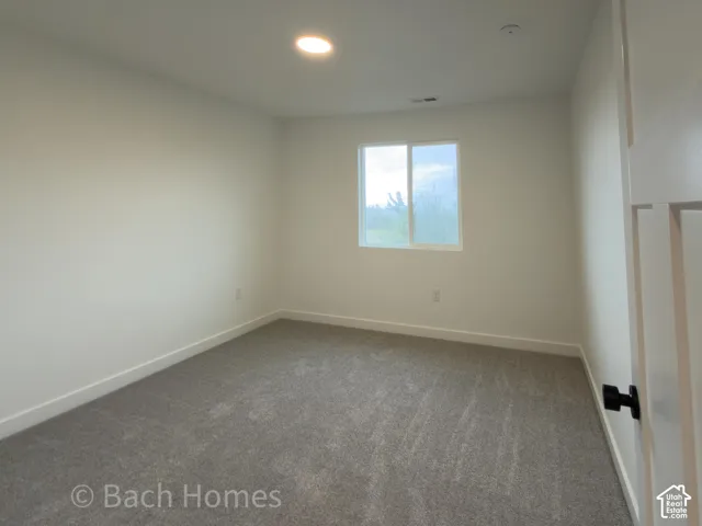 Neutral-toned interior room featuring wall-to-wall carpeting, a single-pane sliding window, recessed ceiling lighting, and a door with matte black hardware
