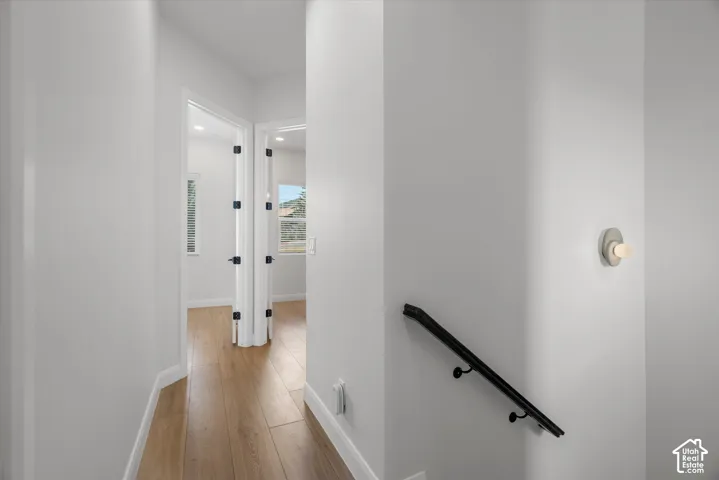 Hallway featuring light wood-finish flooring, white baseboards, and a contemporary wall sconce