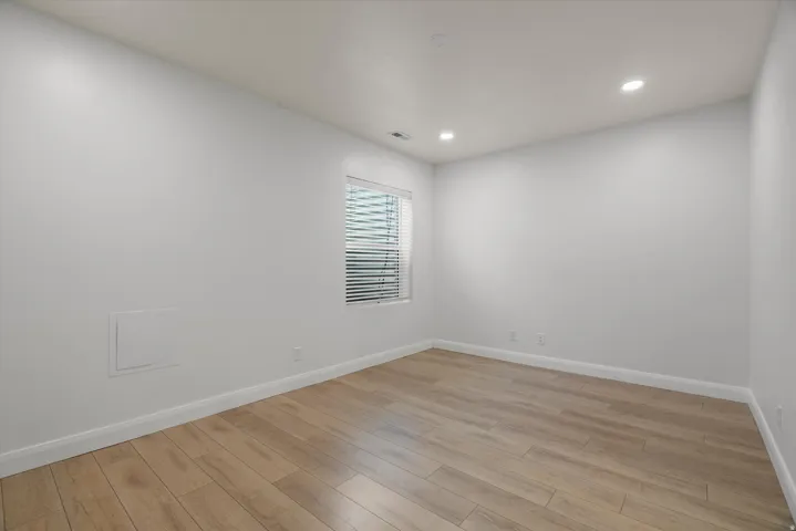Spacious room featuring light wood-finish flooring, white baseboards, and neutral wall paint