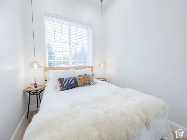 Light-filled room featuring a large window with blinds, wood-finish flooring, and crisp white walls