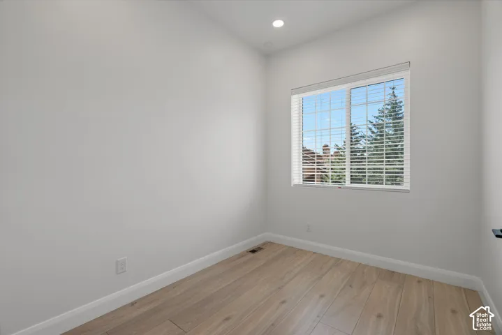 Bright room with wood-finish flooring, white baseboards, a recessed ceiling light, and a window with horizontal blinds