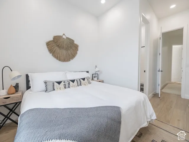 Bright bedroom featuring recessed lighting, light wood-finish flooring, white walls, and a black metal bed frame