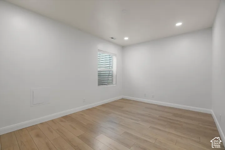 Spacious room featuring light wood-finish flooring, white baseboards, and neutral wall paint