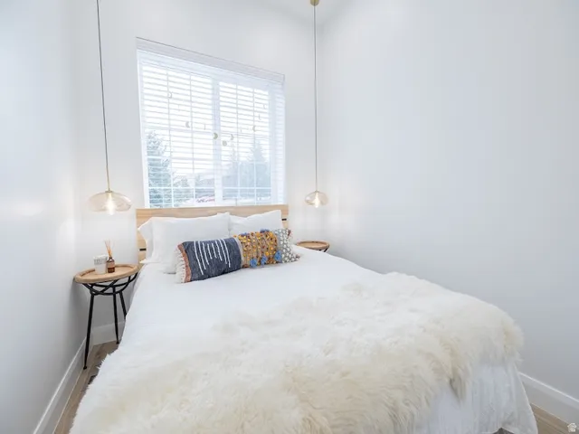 Light-filled room featuring a large window with blinds, wood-finish flooring, and crisp white walls