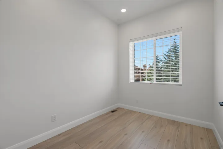Bright room with wood-finish flooring, white baseboards, a recessed ceiling light, and a window with horizontal blinds