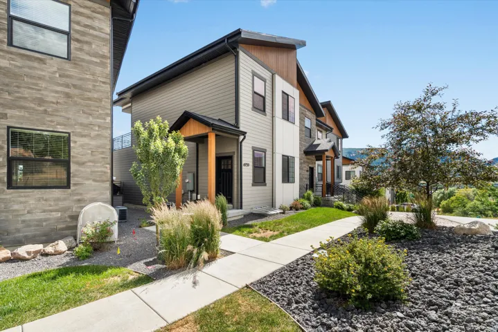 Contemporary multi-level exterior featuring horizontal siding, stone veneer accents, an inviting entryway with a wood-clad support beam, and a paved walkway