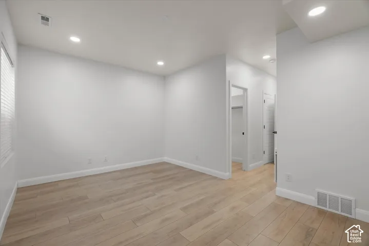 Spacious room featuring light wood-finish flooring, recessed lighting, neutral wall tones, and white baseboards