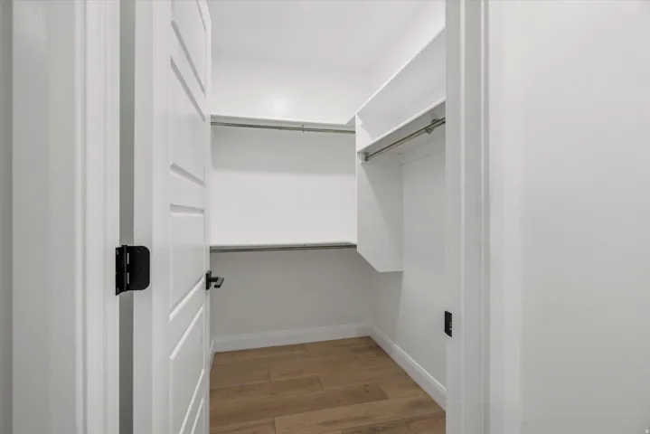 Walk-in closet featuring built-in shelving, hanging rods, and wood-finish flooring