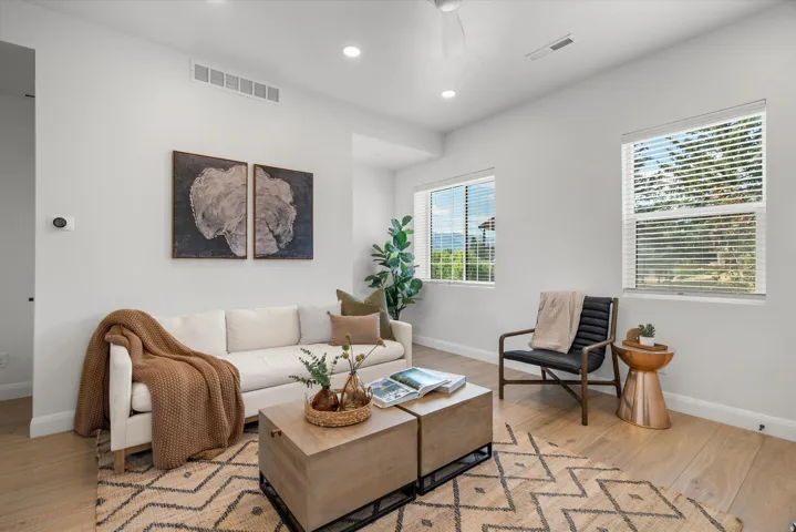 Bright living area featuring wood-finish flooring, recessed lighting, and two windows providing natural light