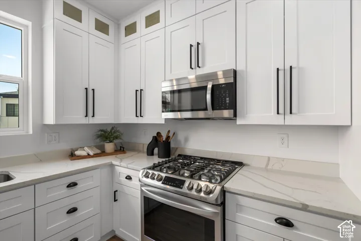 Modern kitchen featuring white shaker cabinetry with black hardware, stainless steel gas range, stainless steel microwave, and light-toned countertops with veining