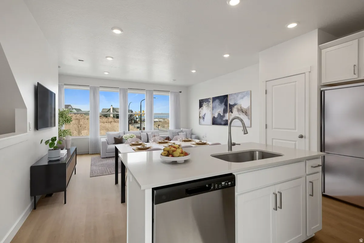 Bright open-concept living area featuring a kitchen island with sink, stainless steel appliances, wood-finish flooring, recessed lighting, and multiple large windows