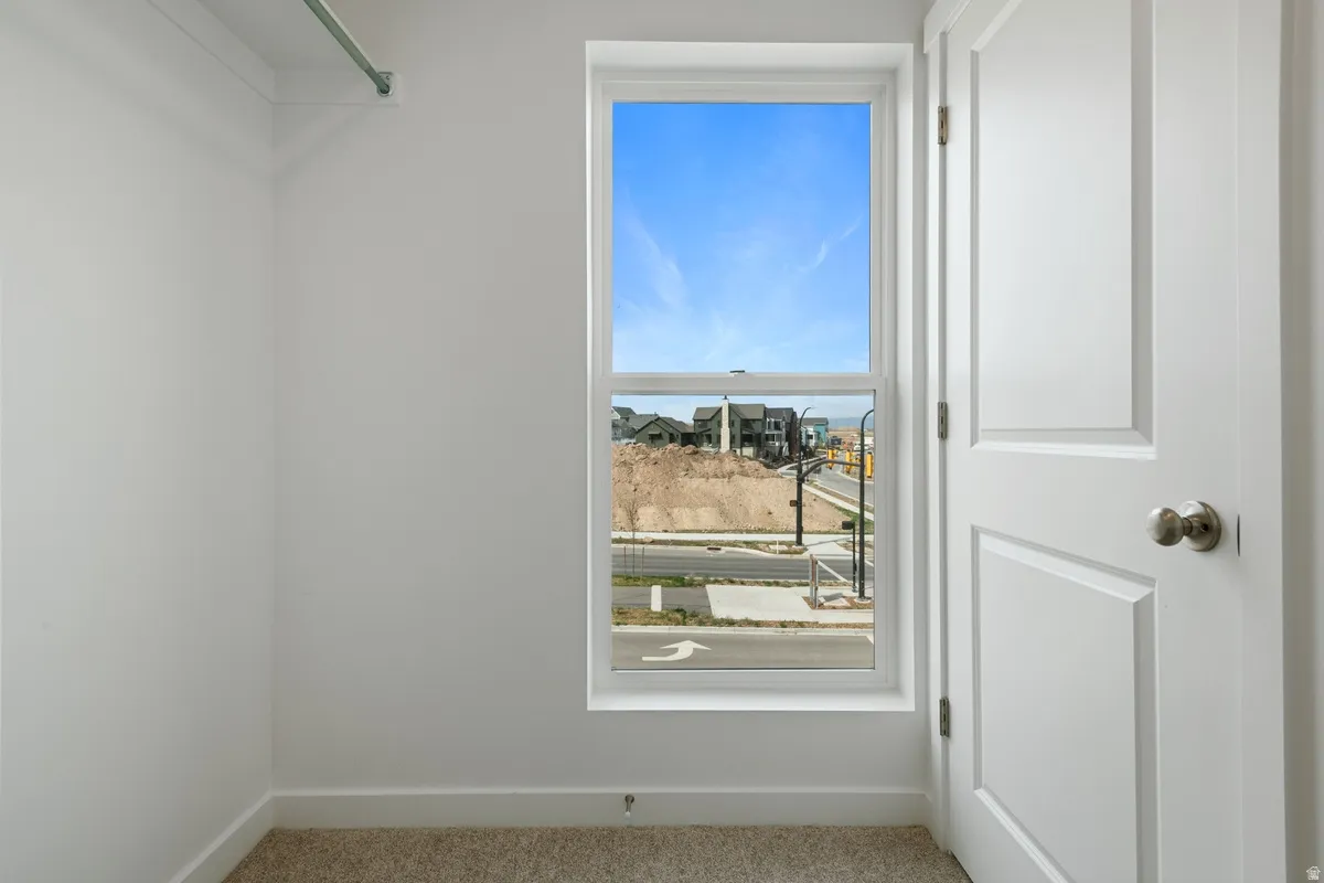 Compact interior space featuring a single window, a white paneled door with brushed nickel hardware, light-colored carpeting, and a clothing rod