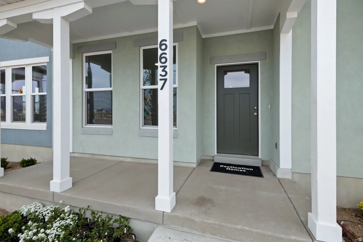 Covered concrete porch with white support columns, showcasing a paneled entry door with a transom window