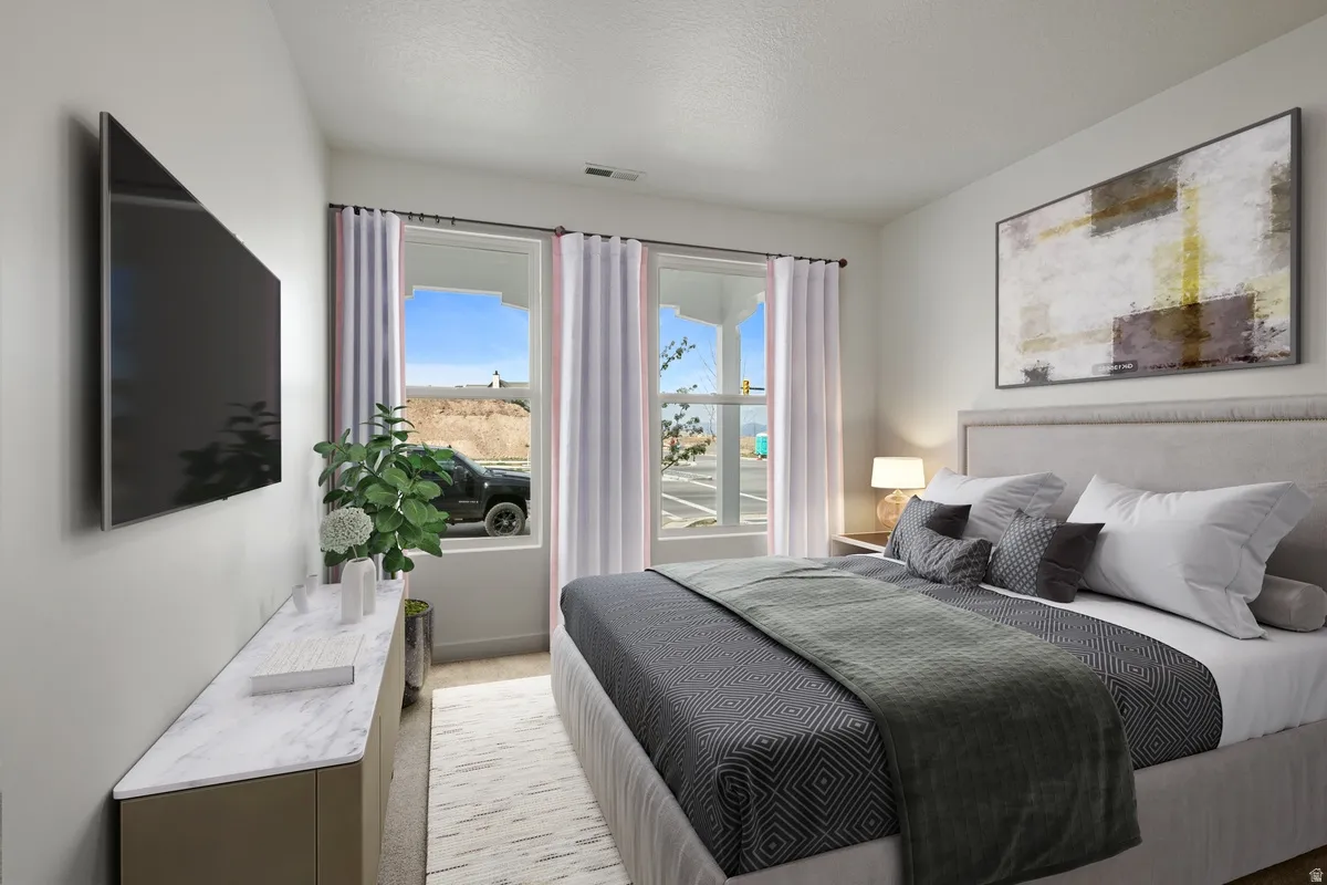 Bedroom featuring dual windows with white curtains, a neutral upholstered headboard, and light-toned walls