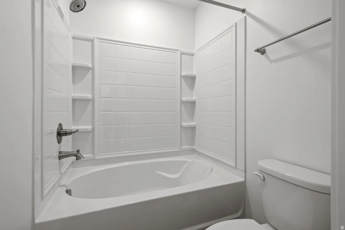 White bathtub with an integrated shower, featuring a tiled surround and built-in shelving