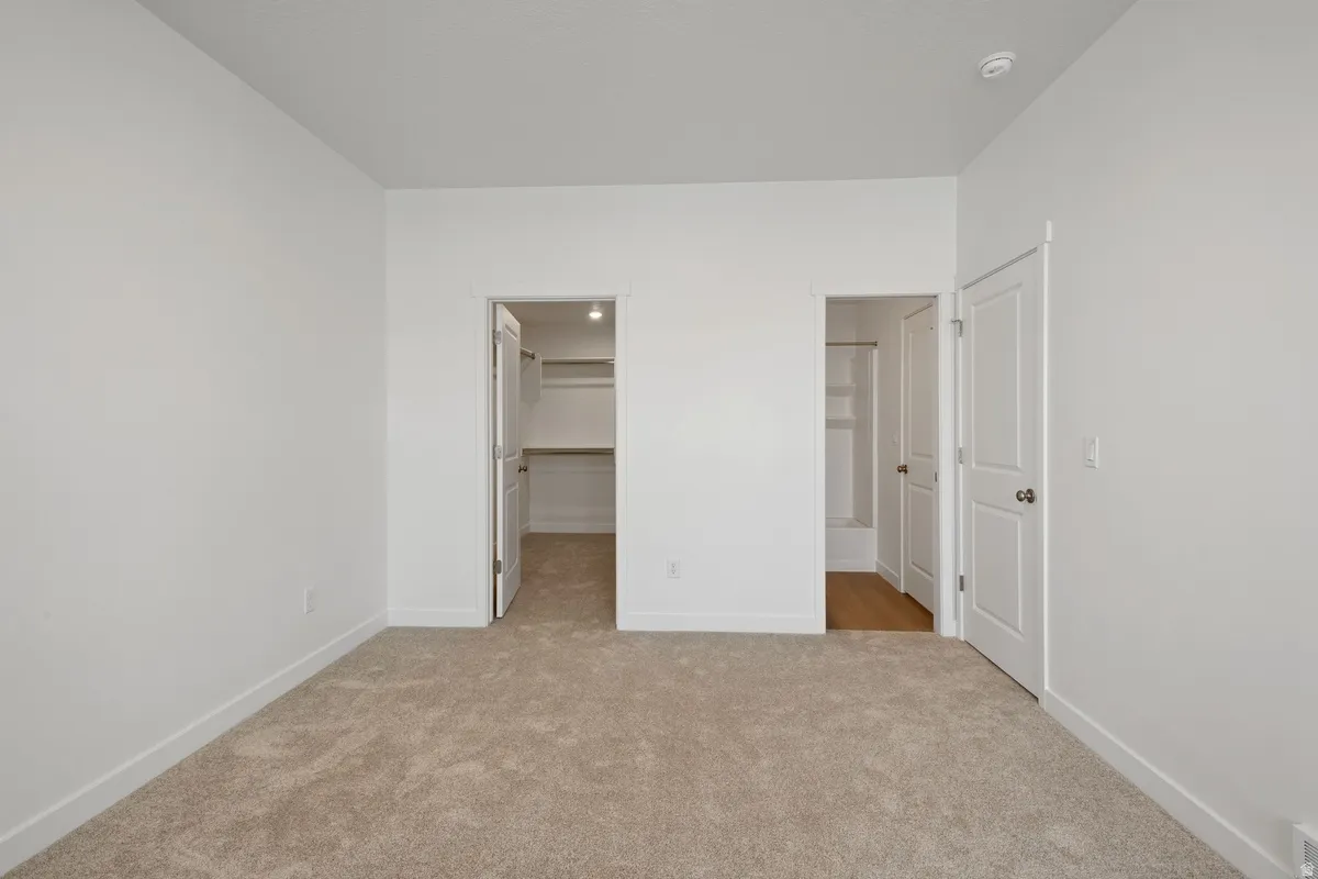 Spacious room featuring neutral carpeting and white painted walls, with two separate doorways