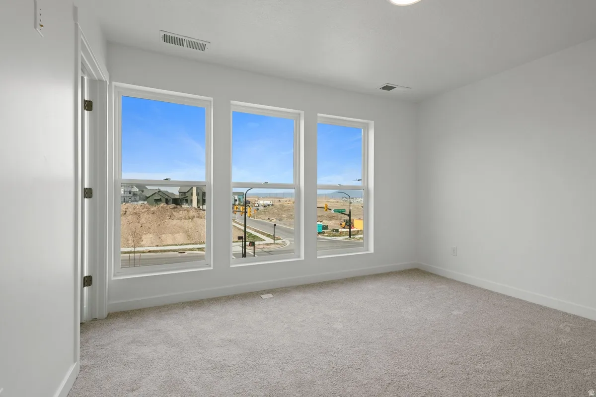 Bright interior space featuring three large windows, white walls, light gray carpeting, and a recessed ceiling light fixture