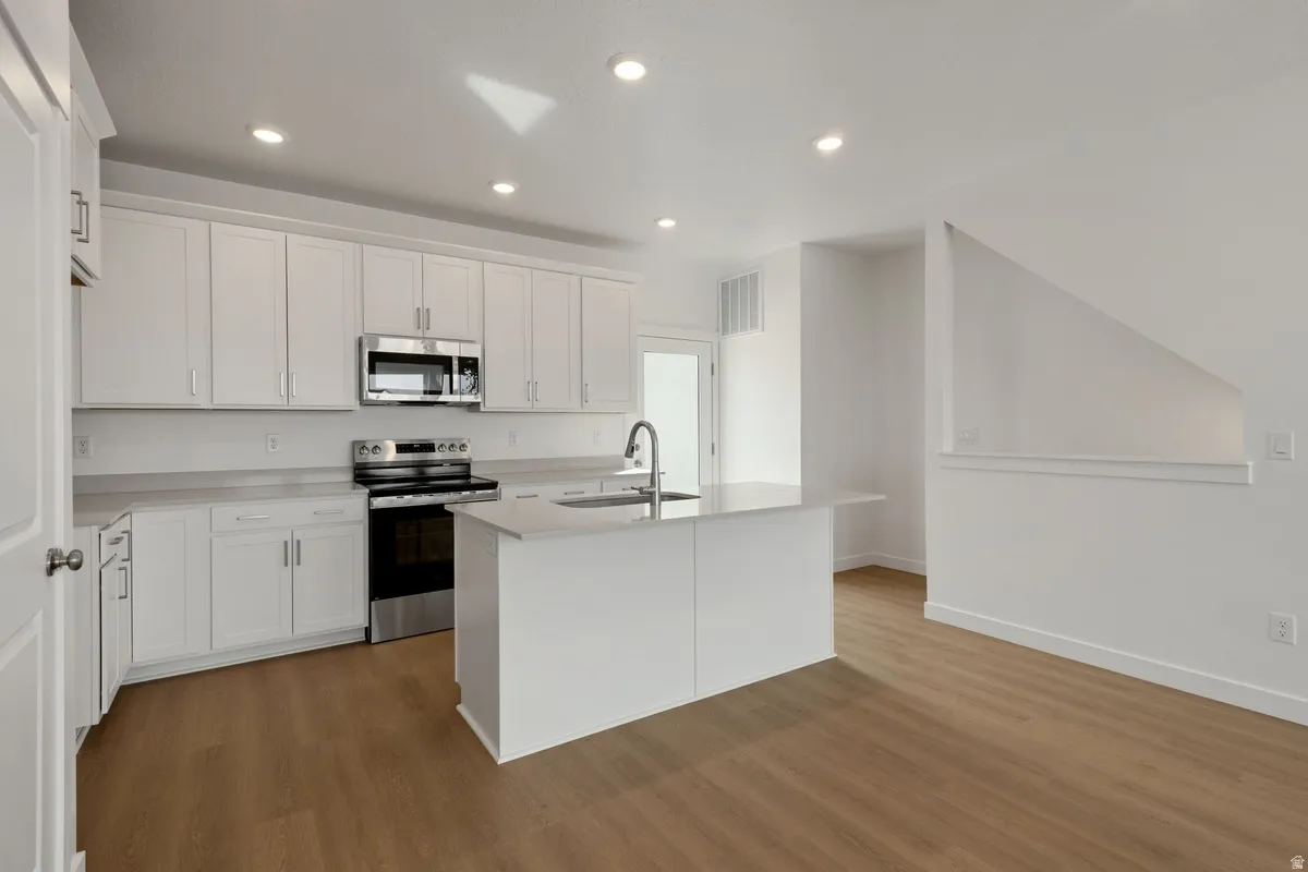 Kitchen featuring white cabinetry, light countertops, wood-finish flooring, stainless steel appliances, and recessed lighting