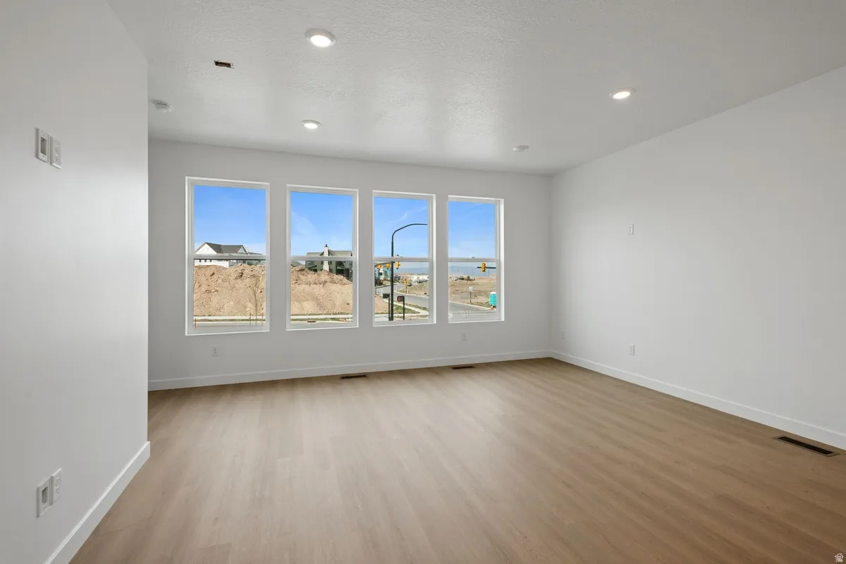 Spacious room featuring multiple large windows, wood-finish flooring, recessed lighting, and crisp white walls with matching baseboards